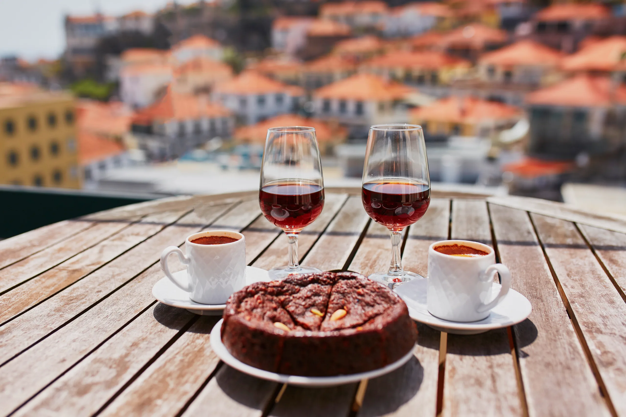 Two glasses of Madeira wine, two cups of fresh espresso coffee and traditional Portuguese honey and nut dessert bolo de mel in cafe with view to Funchal town, Madeira, Portugal