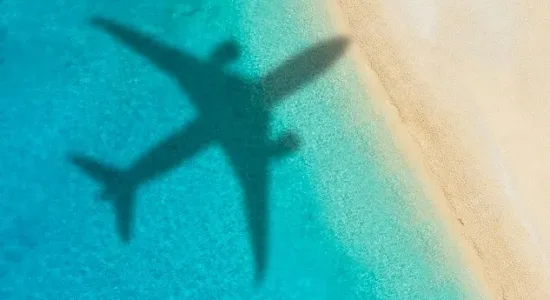 Concept of airplane travel to exotic destination with shadow of commercial airplane flying above beautiful tropical beach. Beach holidays and travel.